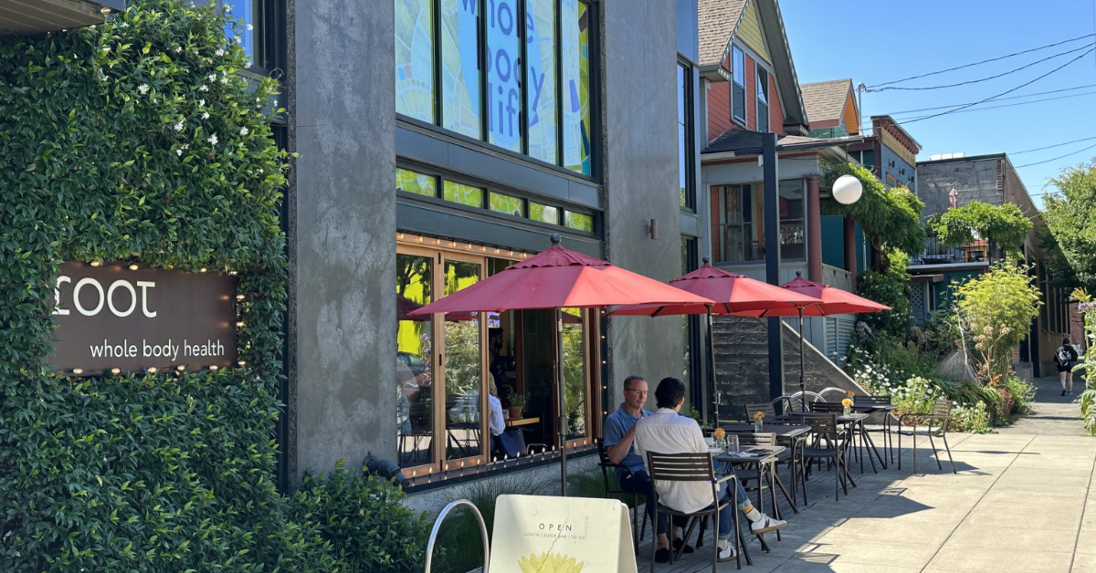 View of the sidewalk cafe and sign at Root Whole Body on a beautiful summer day.